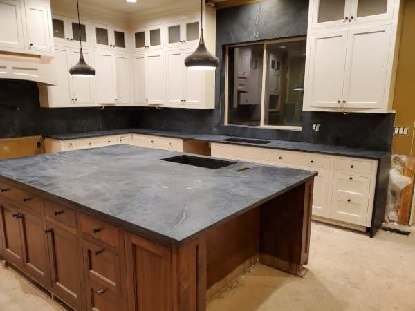Kitchen with white cabinets, brown island, dark countertops, pendant lights.