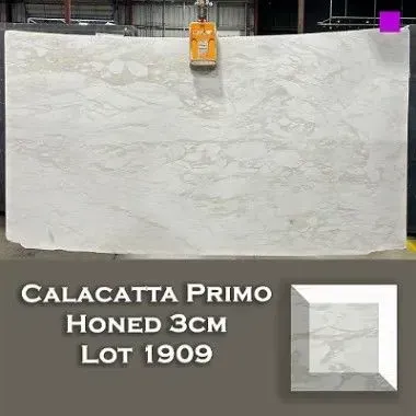 Calacatta Primo Honed marble slab lifted by machinery, with a sample cut and labels.