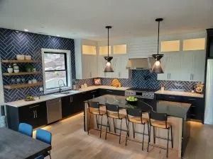 Modern kitchen with dark blue backsplash, two-tone cabinets, island with stools, pendant lights.