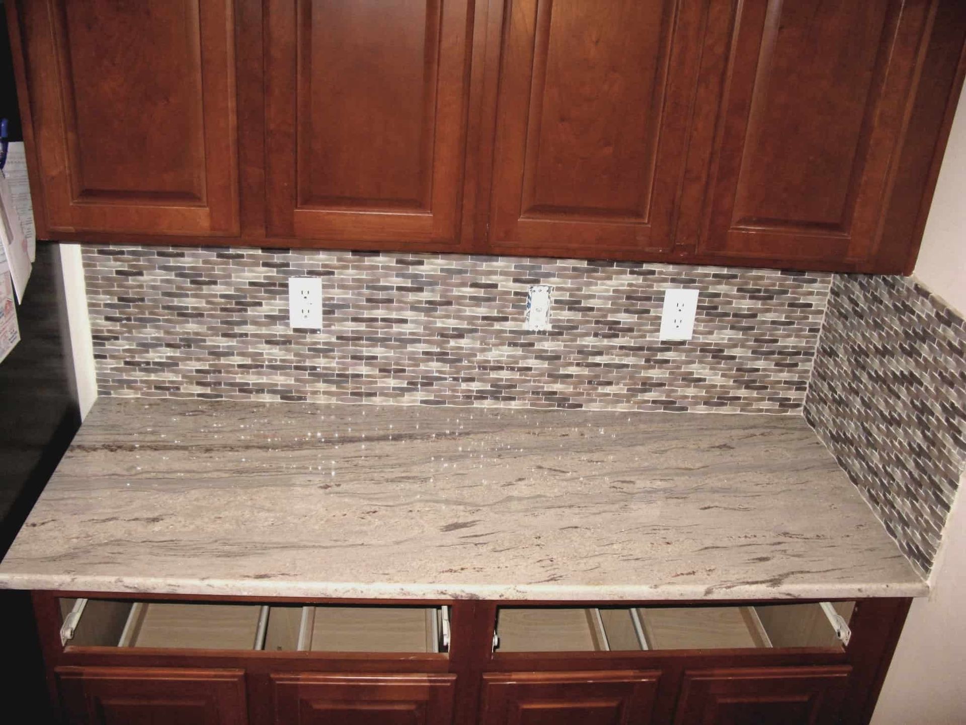 Dark wooden kitchen cabinets with a granite countertop and tiled backsplash.