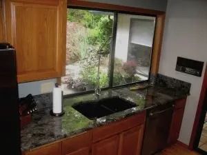 Kitchen with a black sink, granite countertop, wooden cabinets, and a window overlooking greenery.