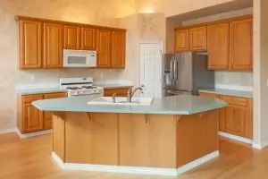 Kitchen with wood cabinets, light blue countertop island, and stainless steel appliances.