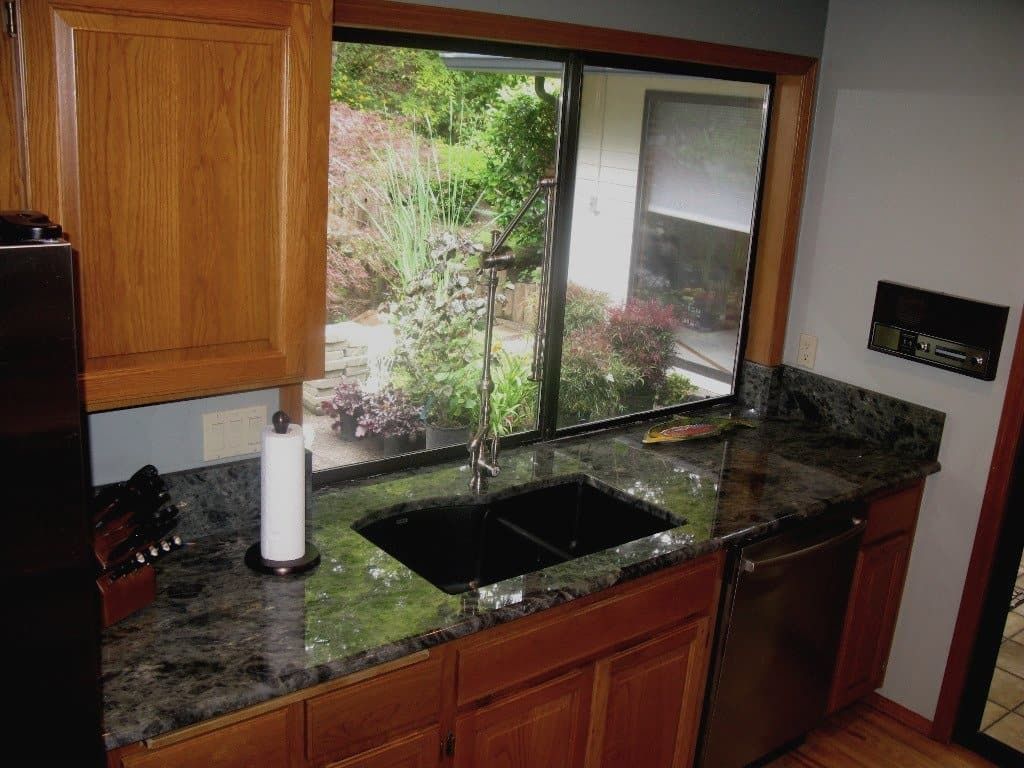 Kitchen with granite countertop, wooden cabinets, a double sink, and a window overlooking greenery.