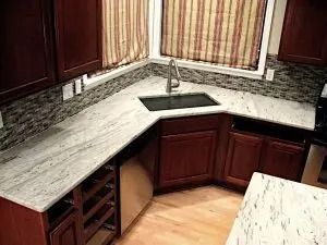 L-shaped kitchen with white granite countertops, dark cabinets, sink, and window.