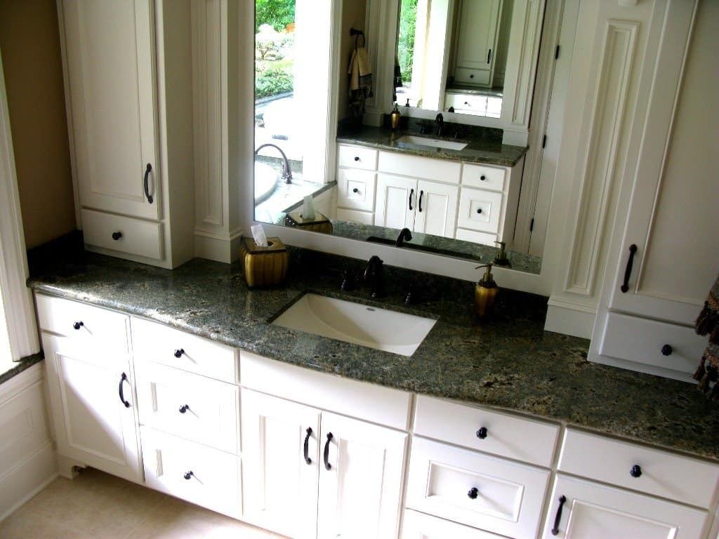 White bathroom cabinets with a dark granite countertop and a large mirror.