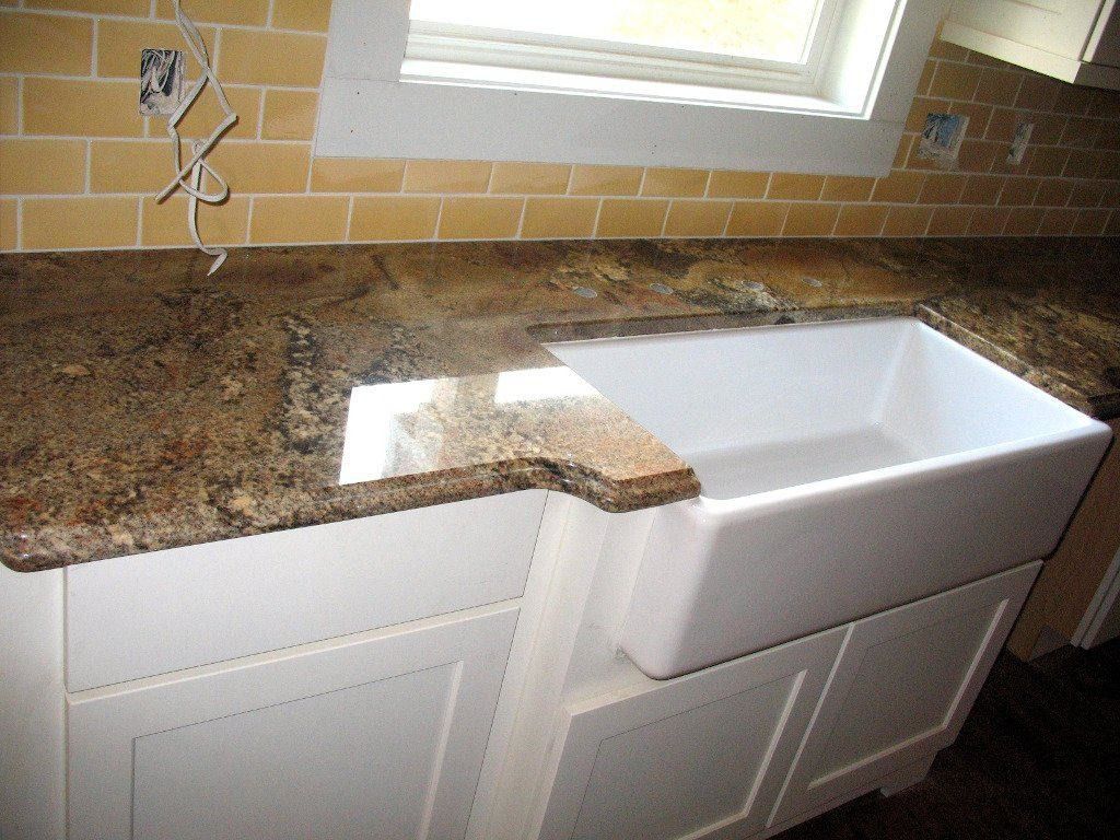 Granite countertop with white farmhouse sink and cabinets against yellow tile backsplash.
