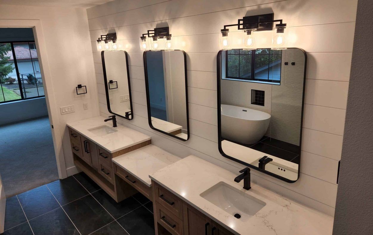 Bathroom with three vanities, mirrors, and a soaking tub reflected in the right mirror.