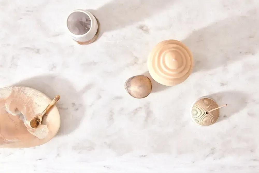Assortment of wooden objects and a plate on a white, textured surface. Includes a spoon, circular bowl, and sphere.