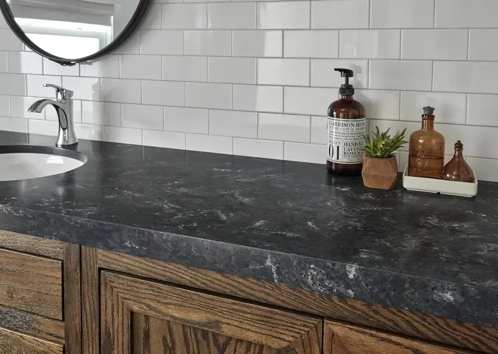 Bathroom vanity with dark countertop, wooden cabinets, white subway tile backsplash, and decorative items.