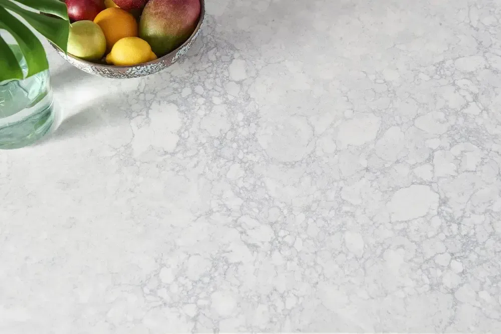 Fruit bowl on a textured white surface; a clear vase with a leaf on the left.