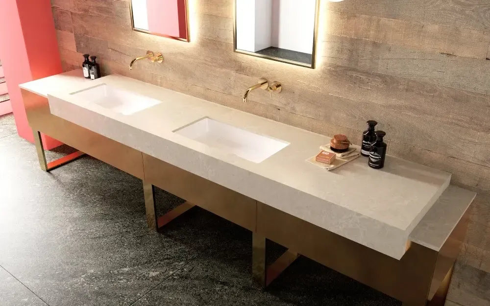 Long, beige bathroom vanity with two sinks, gold legs, and matching fixtures.