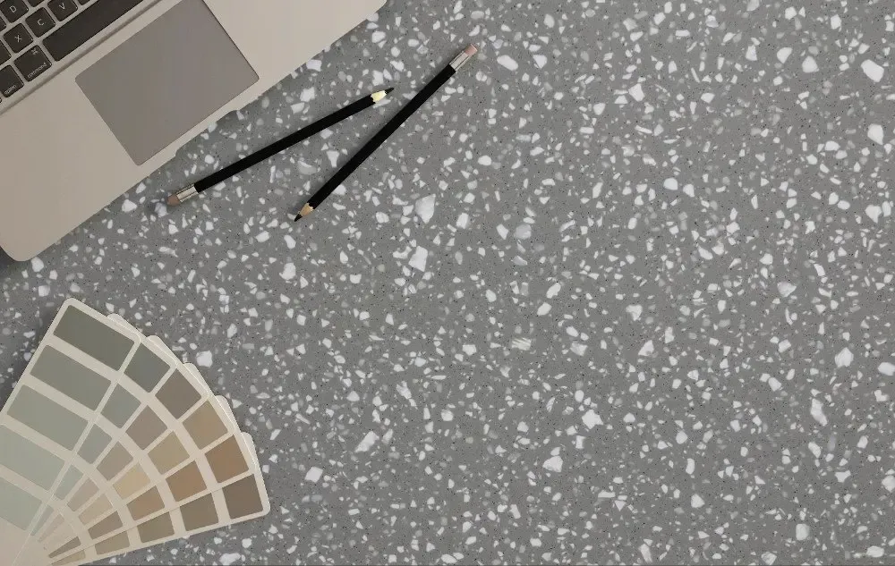 Laptop, pencils, and paint swatches on a speckled gray surface, likely an interior design workspace.