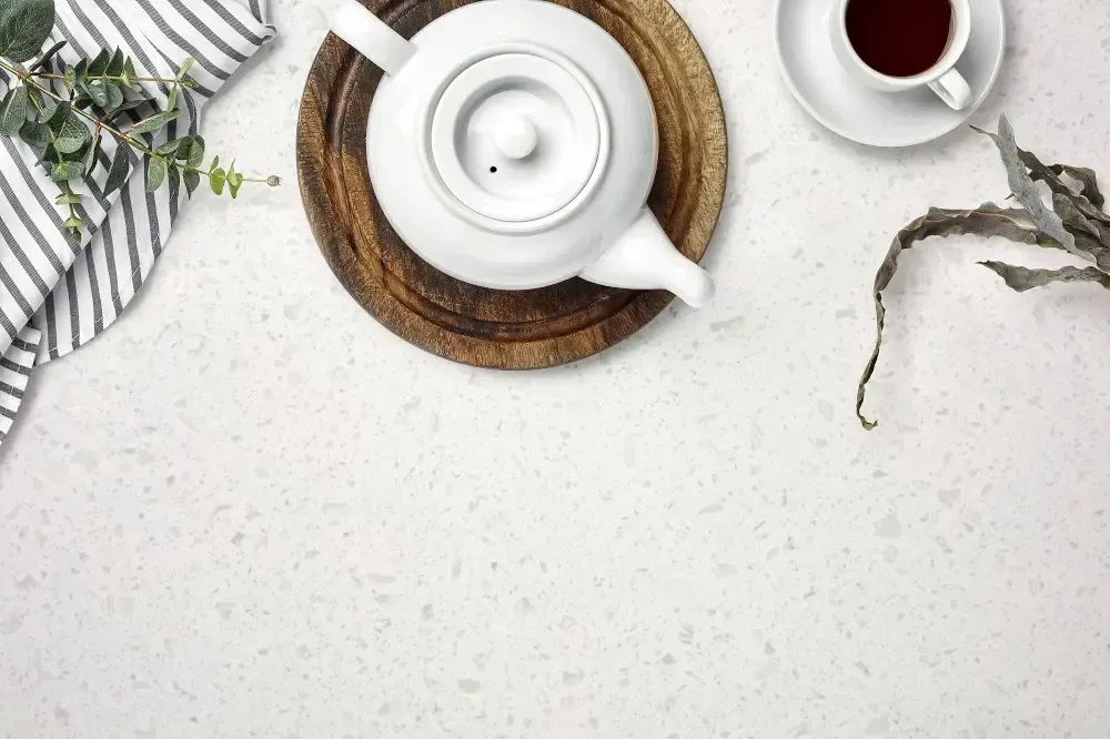 White teapot, cup of tea, wooden board, and striped cloth on a white surface.