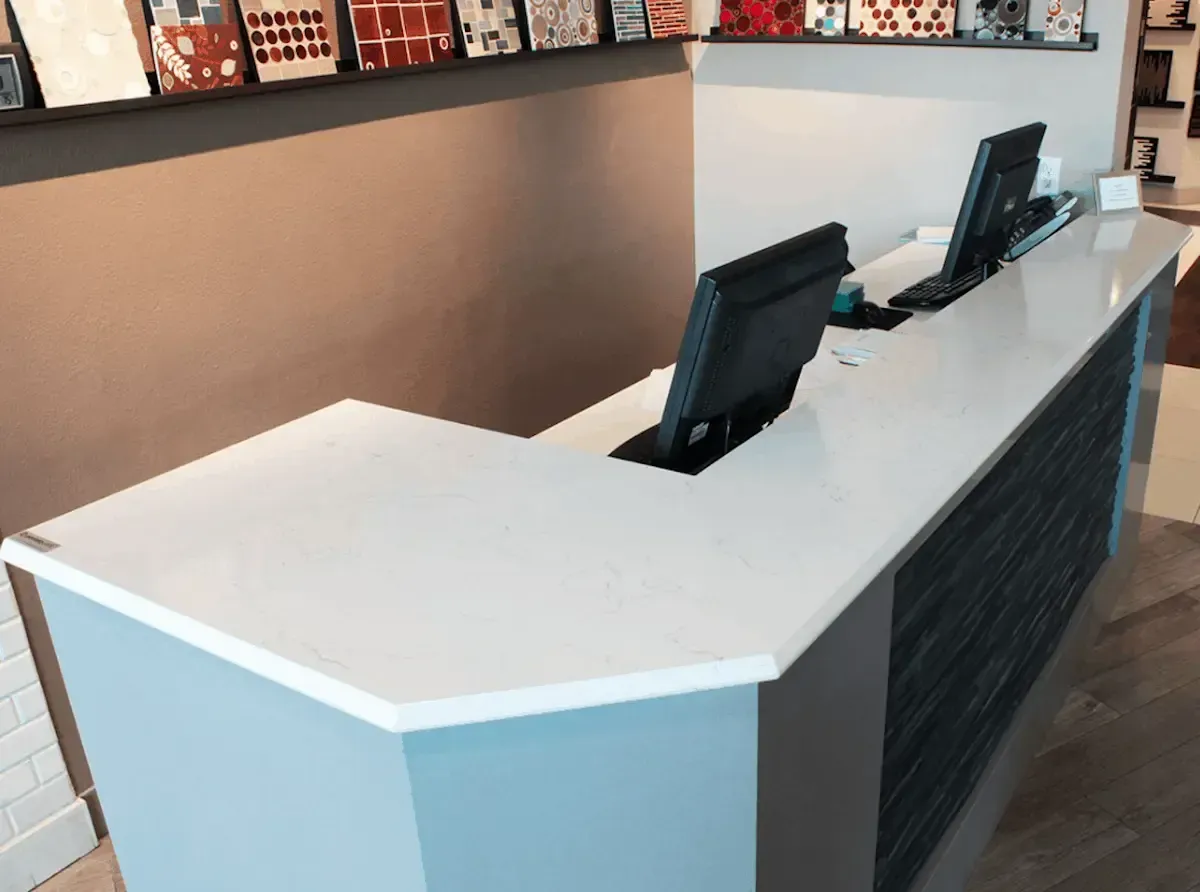 A modern reception desk with a white countertop, two computer monitors, and a blue and gray exterior.