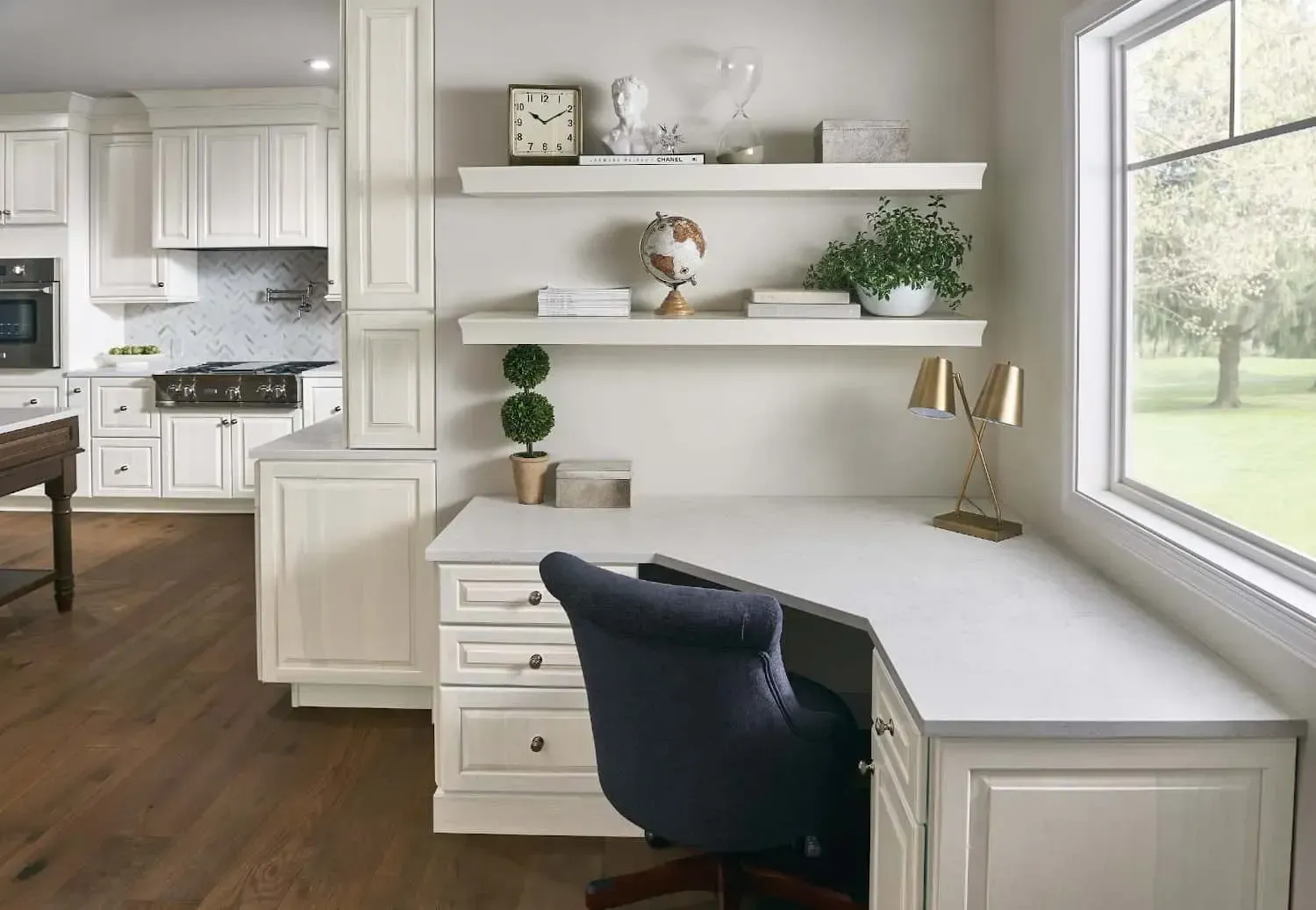 Home office with a white desk, shelves, and a blue chair, overlooking a green yard through a large window.