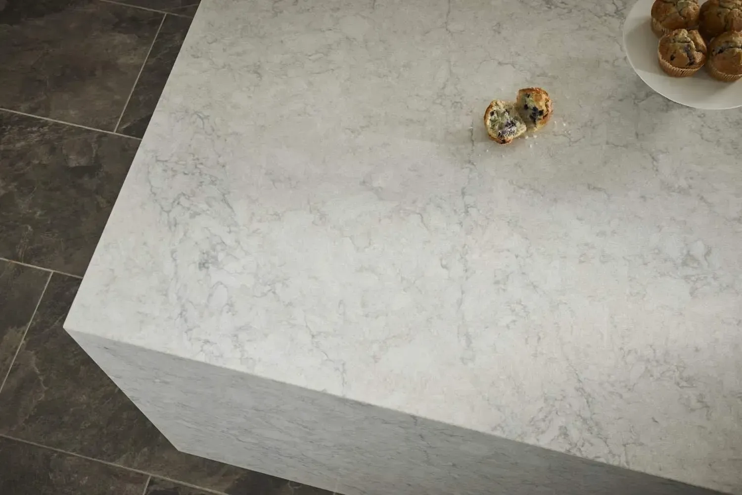 Light gray countertop with marble effect, treats and plate on top, dark tiled floor.
