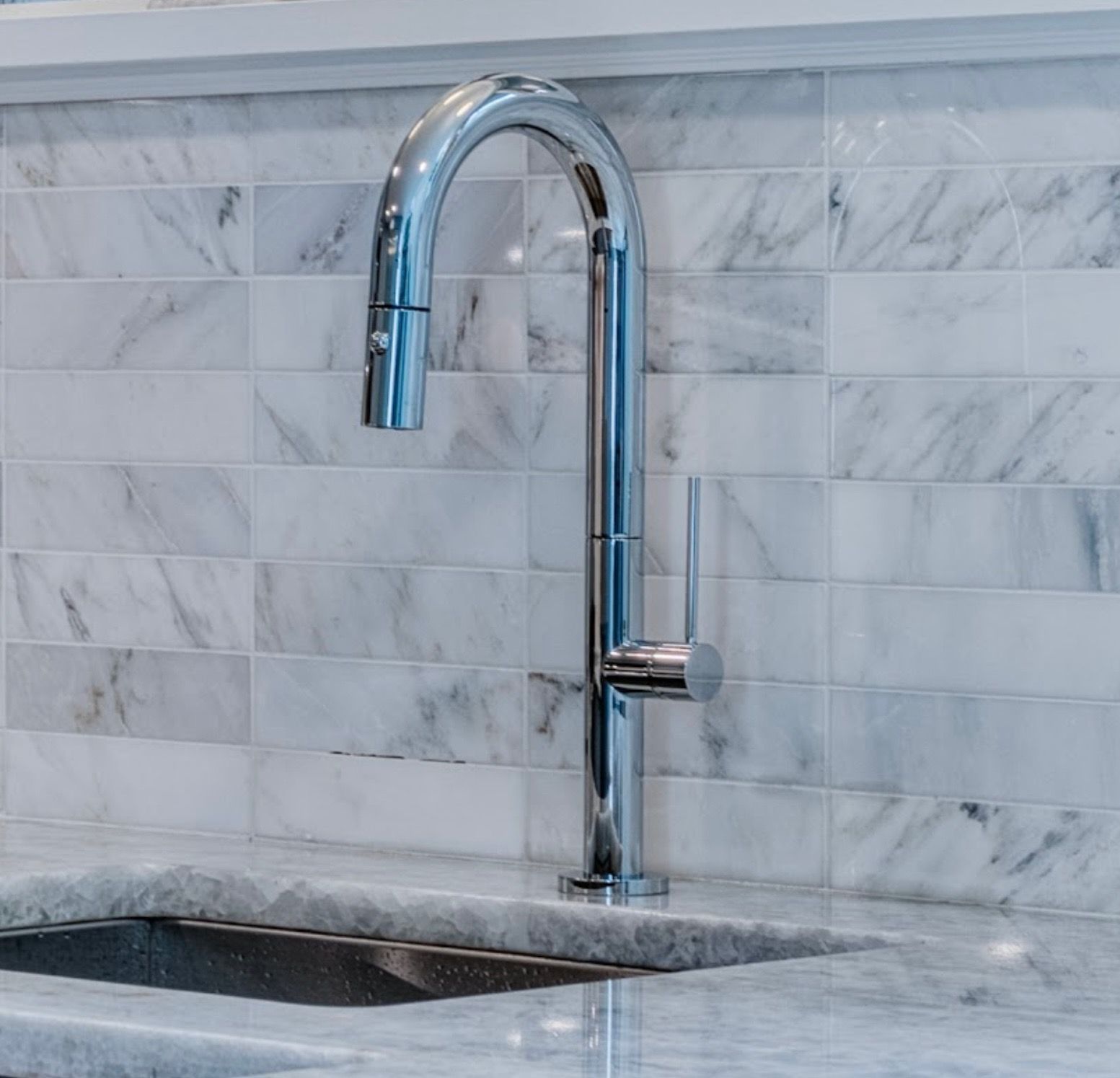 A kitchen sink with a chrome faucet and marble tiles.