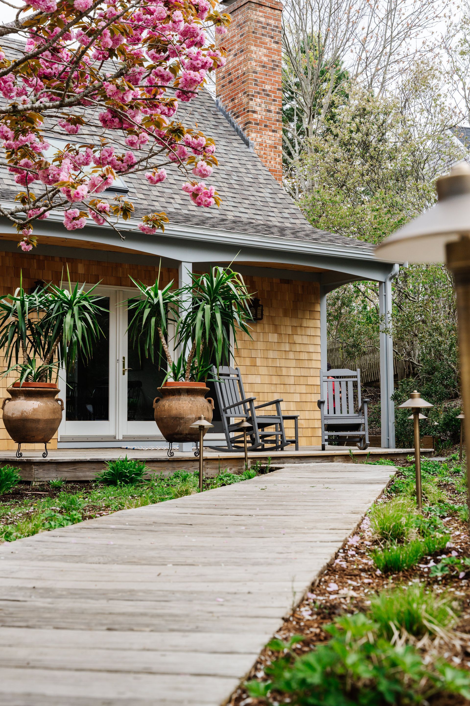 A wooden walkway leading to a house with a porch and rocking chairs.
