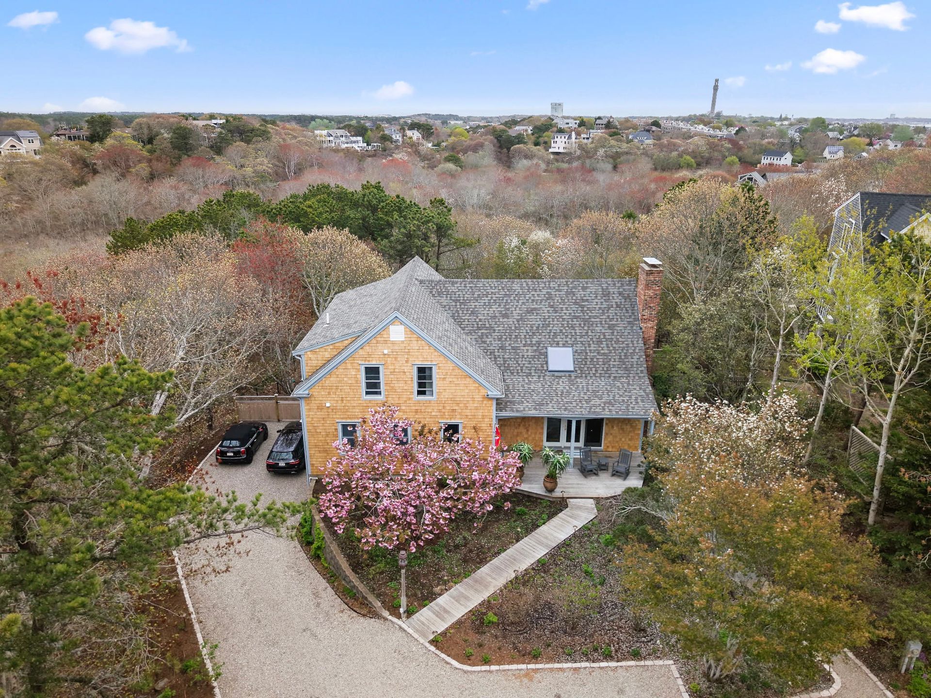 An aerial view of a house with cars parked in front of it surrounded by trees.