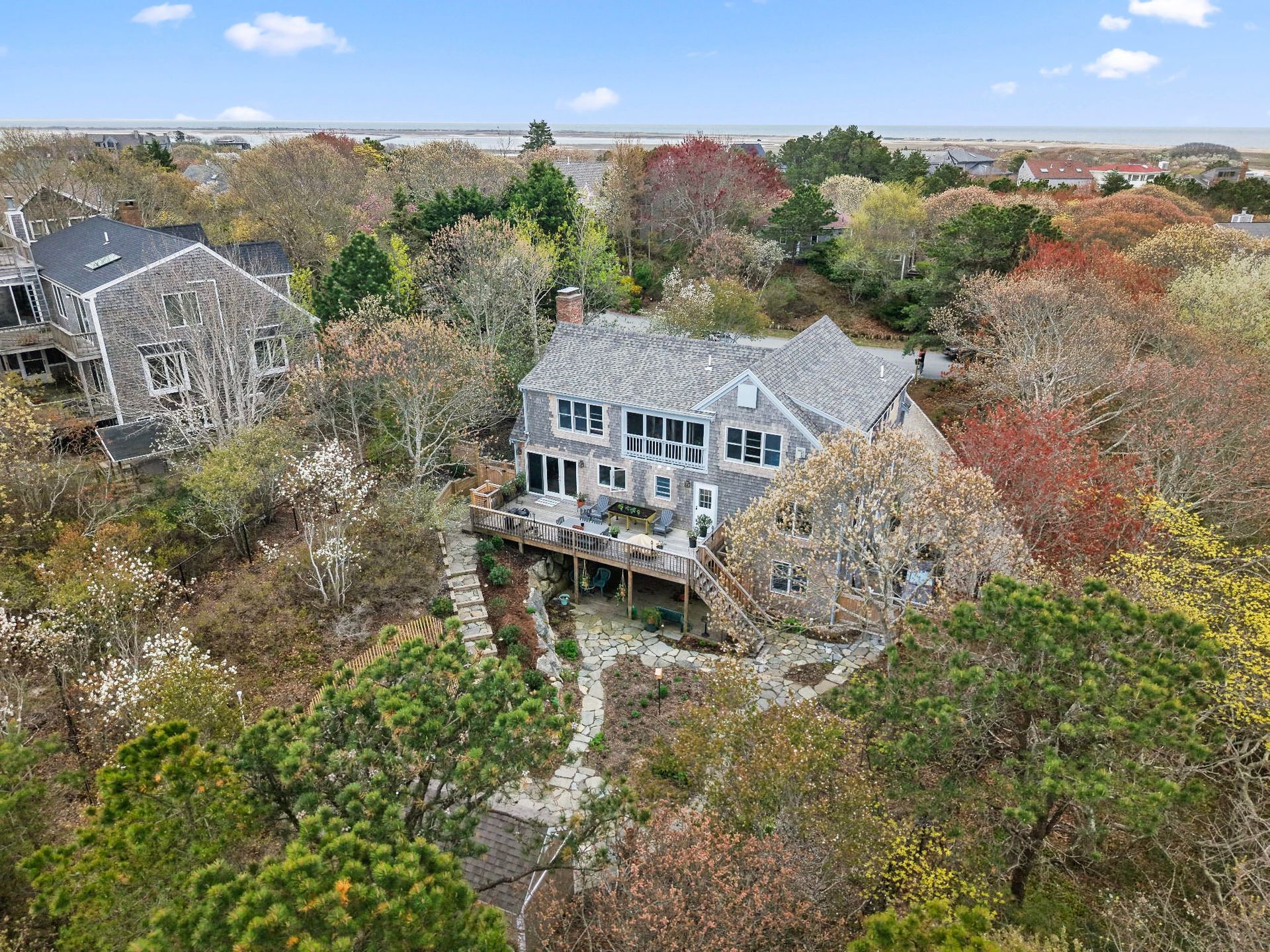 Gray house surrounded by trees and a small deck, in a wooded area.