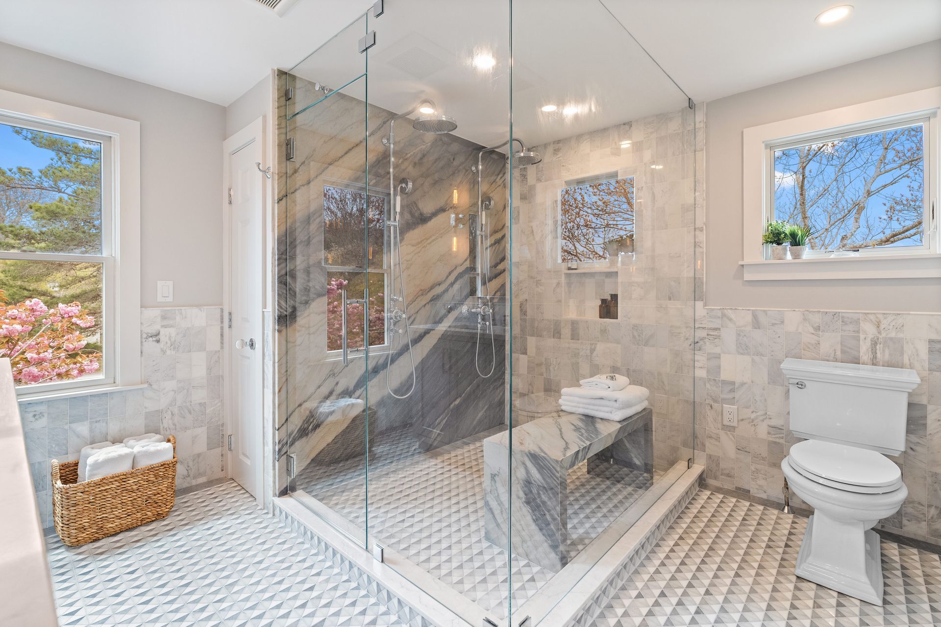 A bathroom with a walk in shower, toilet, sink, and window.