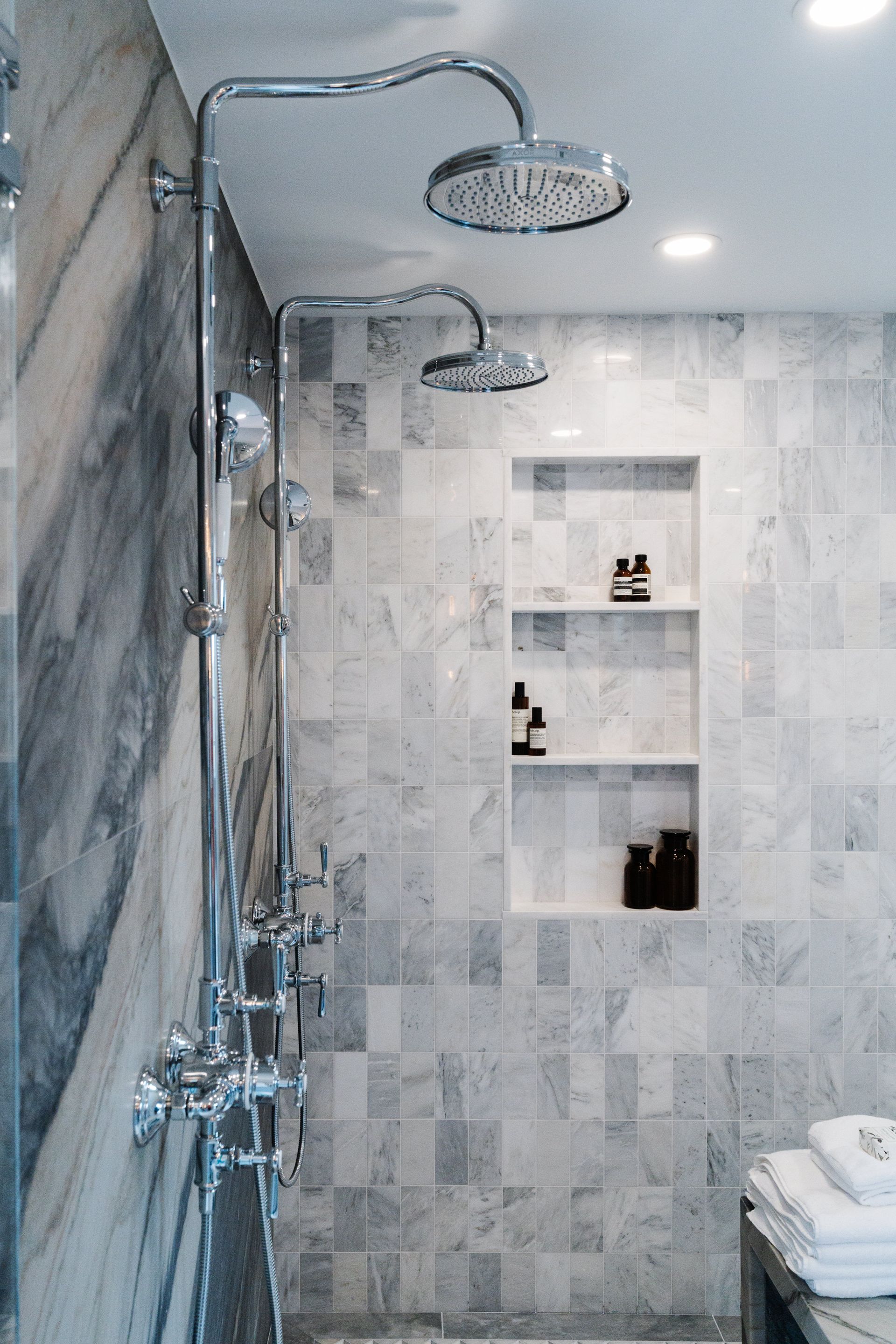A bathroom with two shower heads and a shelf.
