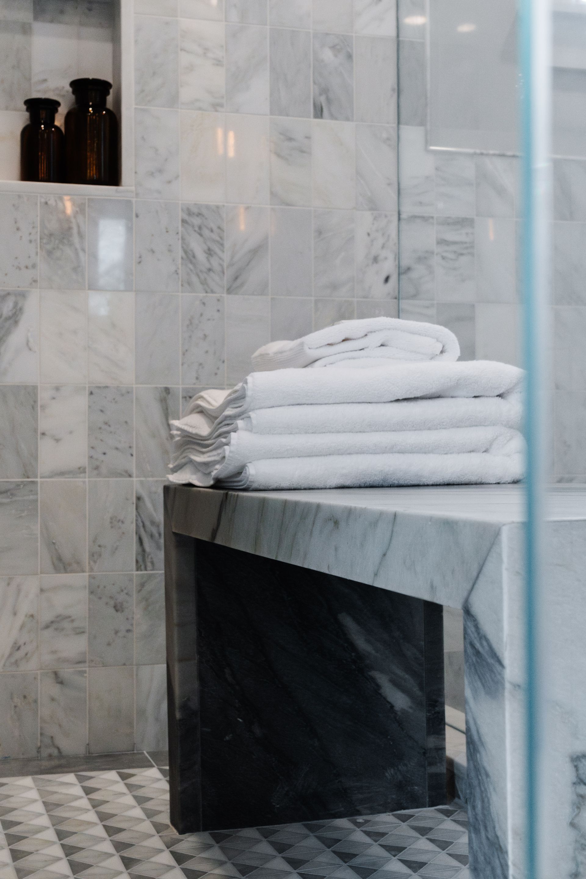 A bathroom with marble tiles and a bench with towels on it.