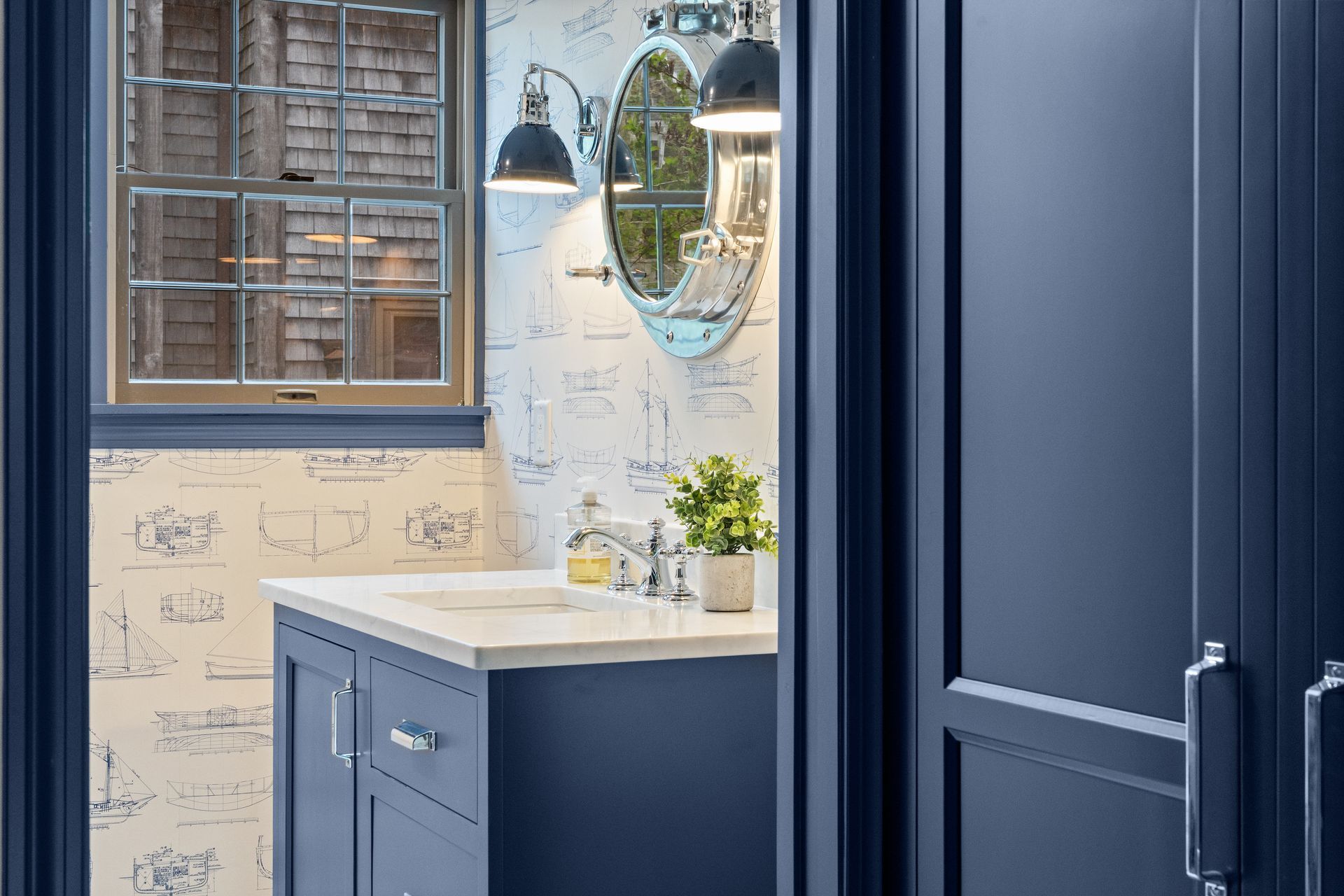 A bathroom with blue cabinets, a sink, a mirror, and a window.