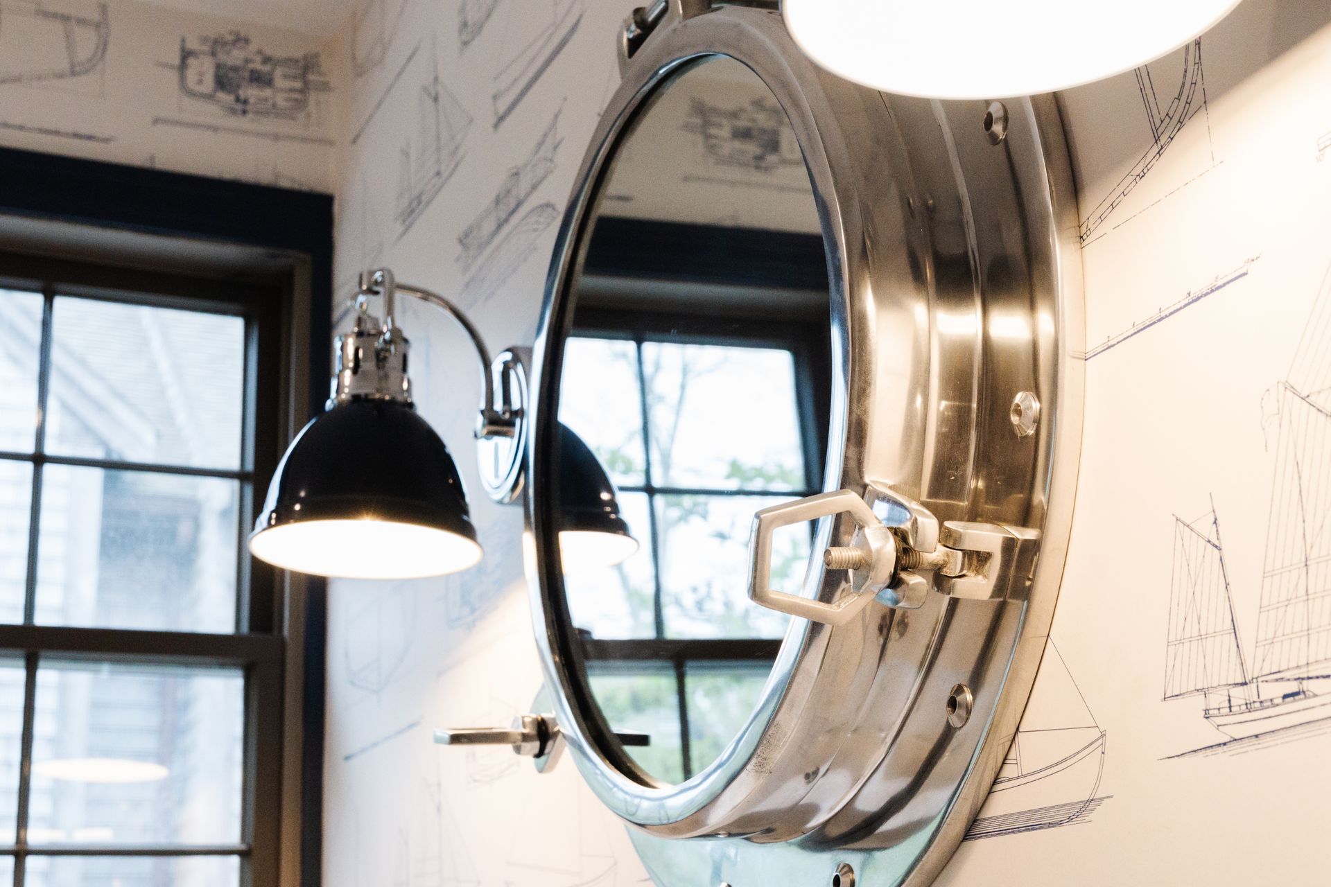 Round mirror is hanging on a wall next to a window.