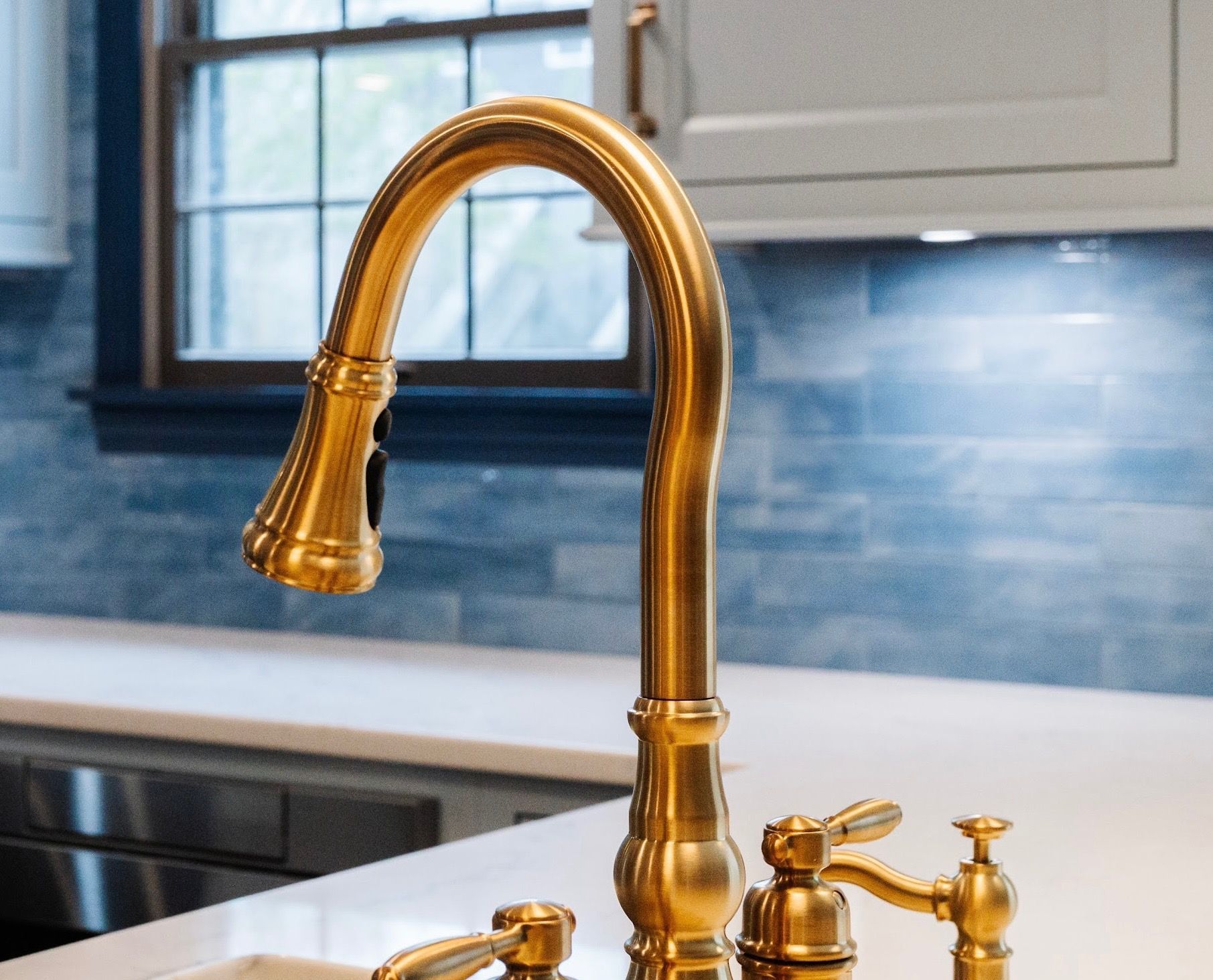 A kitchen sink with a gold faucet and a window in the background