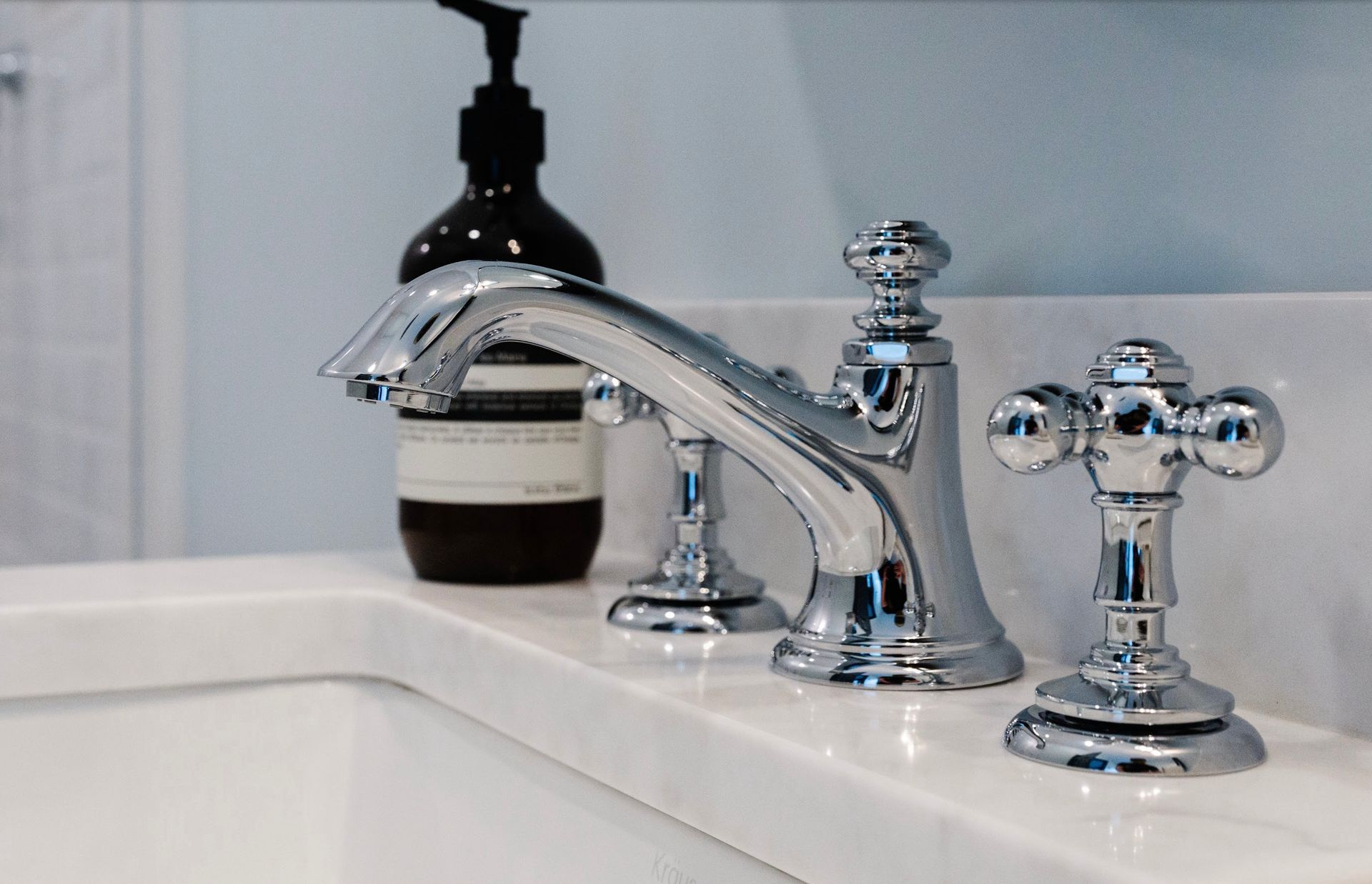 A bathroom sink with chrome faucets and a bottle of soap on the counter.
