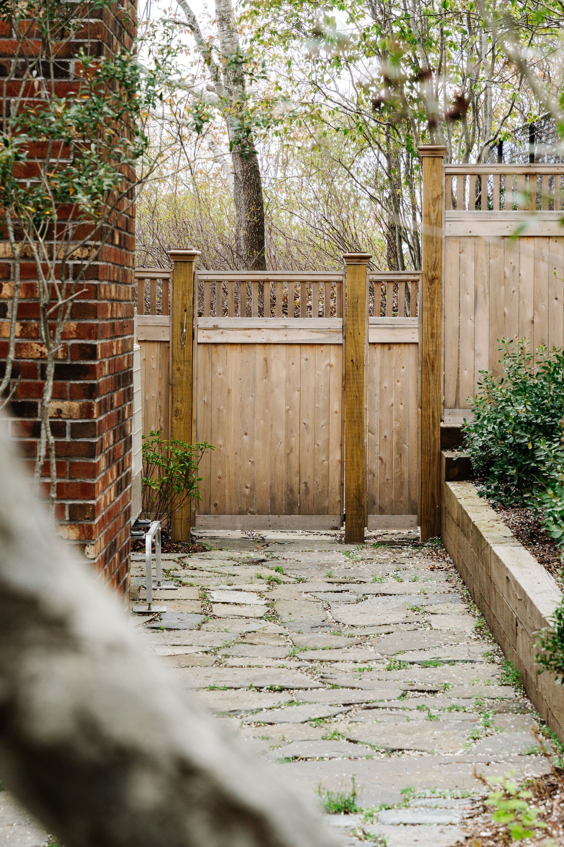 A wooden fence surrounds a stone walkway in a backyard.