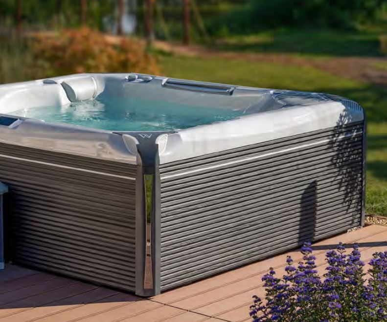 A hot tub is sitting on a wooden deck next to purple flowers.