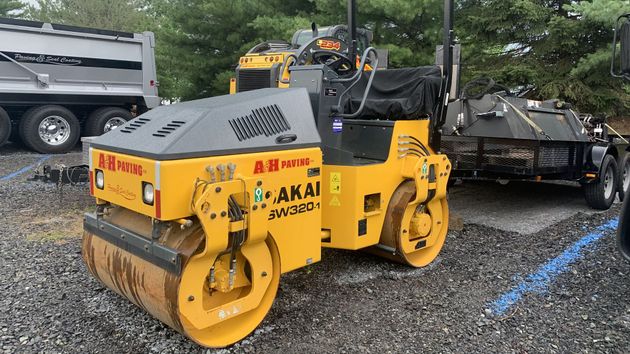 Yellow road roller parked on gravel beside construction trucks and equipment