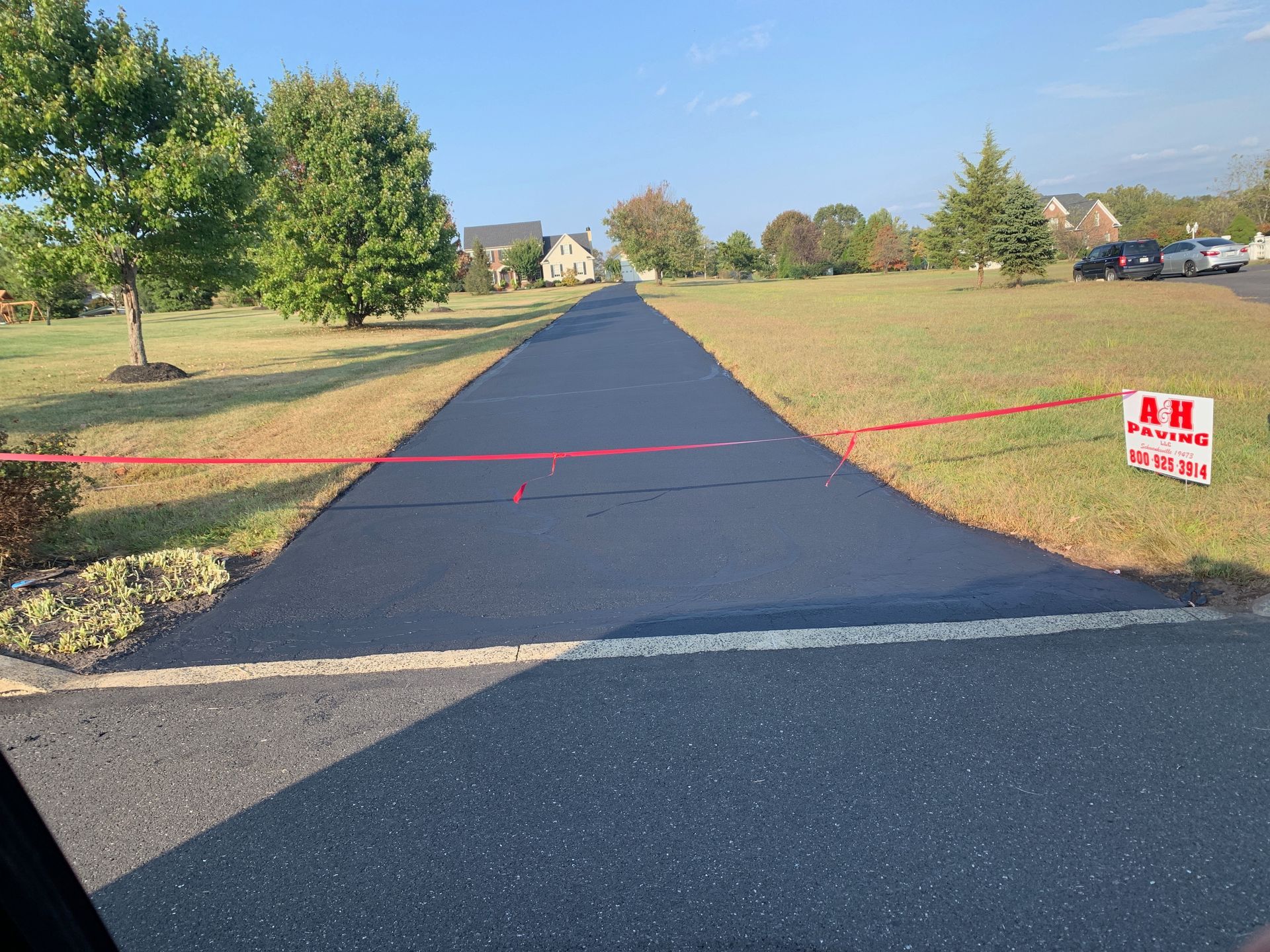 Rural paved road blocked by red tape, with a no entry sign on the right and houses in the distance