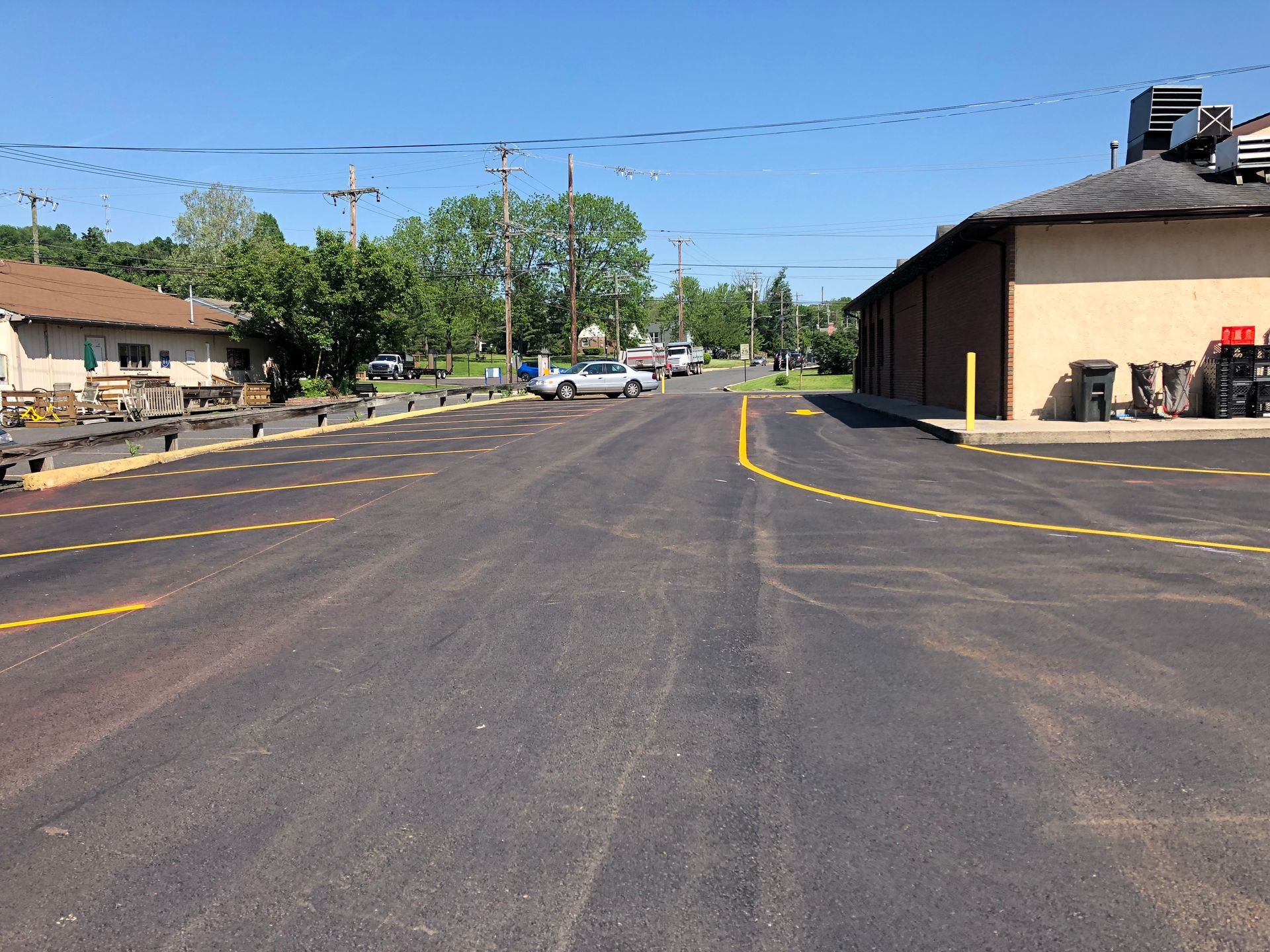Wide asphalt road with yellow lines beside buildings and trees under a clear blue sky.