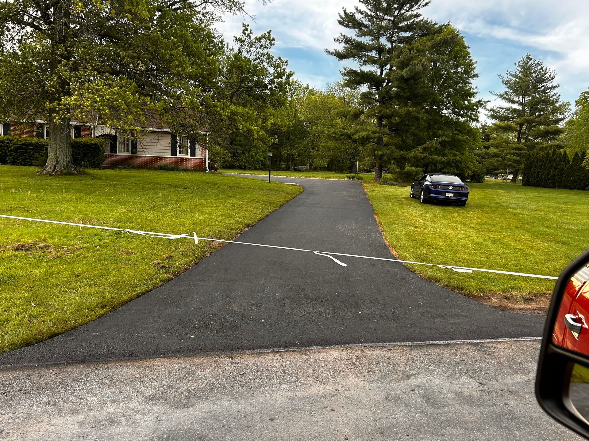 Curved driveway leading to a brick house, with a parked car and green lawn on a cloudy day