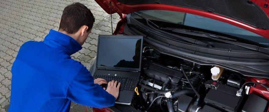 A man is working on a car engine with a laptop.