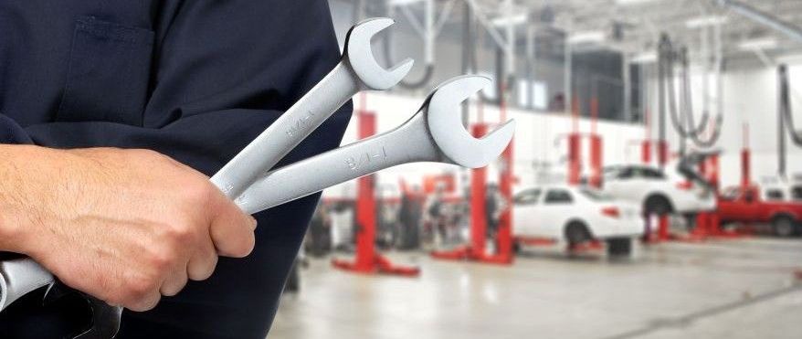 A man is holding two wrenches in a garage.