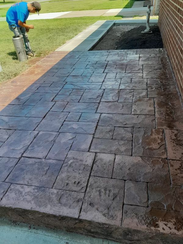A man is working on a concrete walkway next to a brick building