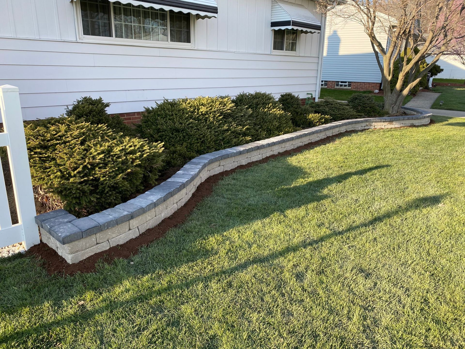 A lawn with a brick wall and bushes in front of a house.