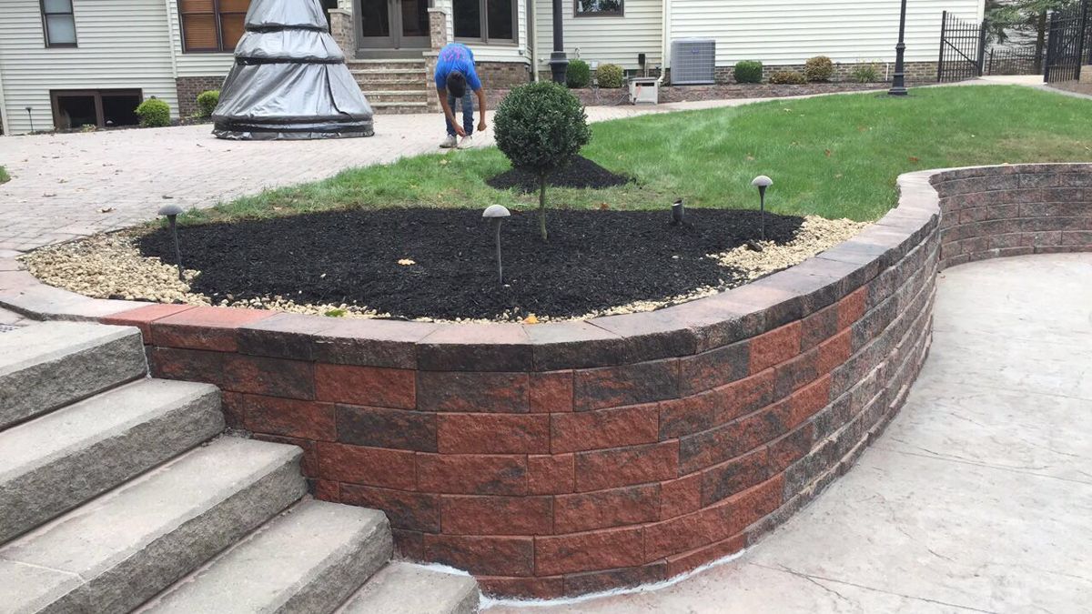 A man is standing next to a brick wall in a yard.