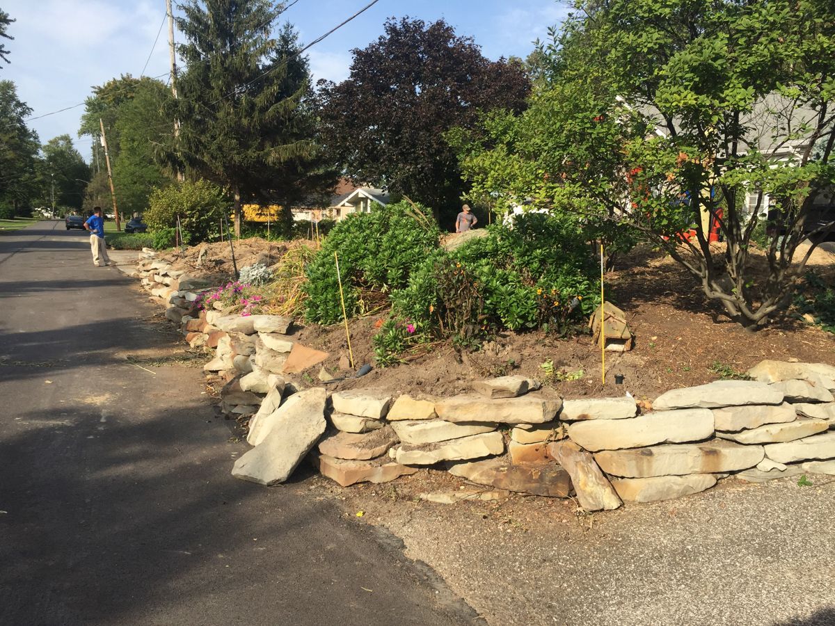 A person is walking down a street next to a stone wall.
