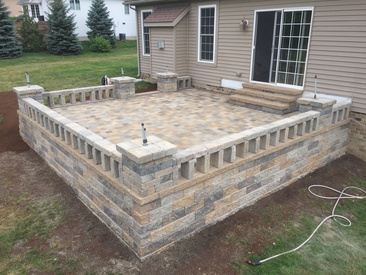 A patio with a brick wall and a bench in front of a house.
