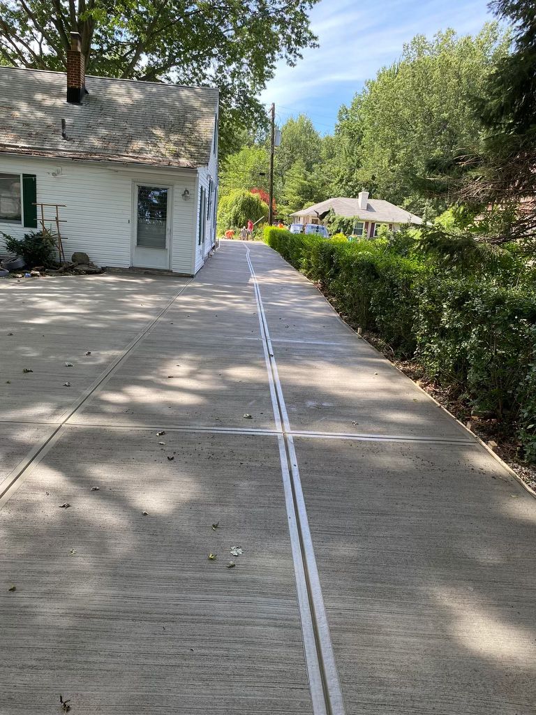 A concrete driveway leading to a white house.