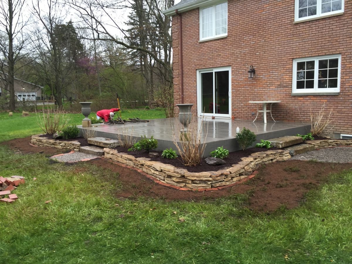 A man is working on a patio in front of a brick house.