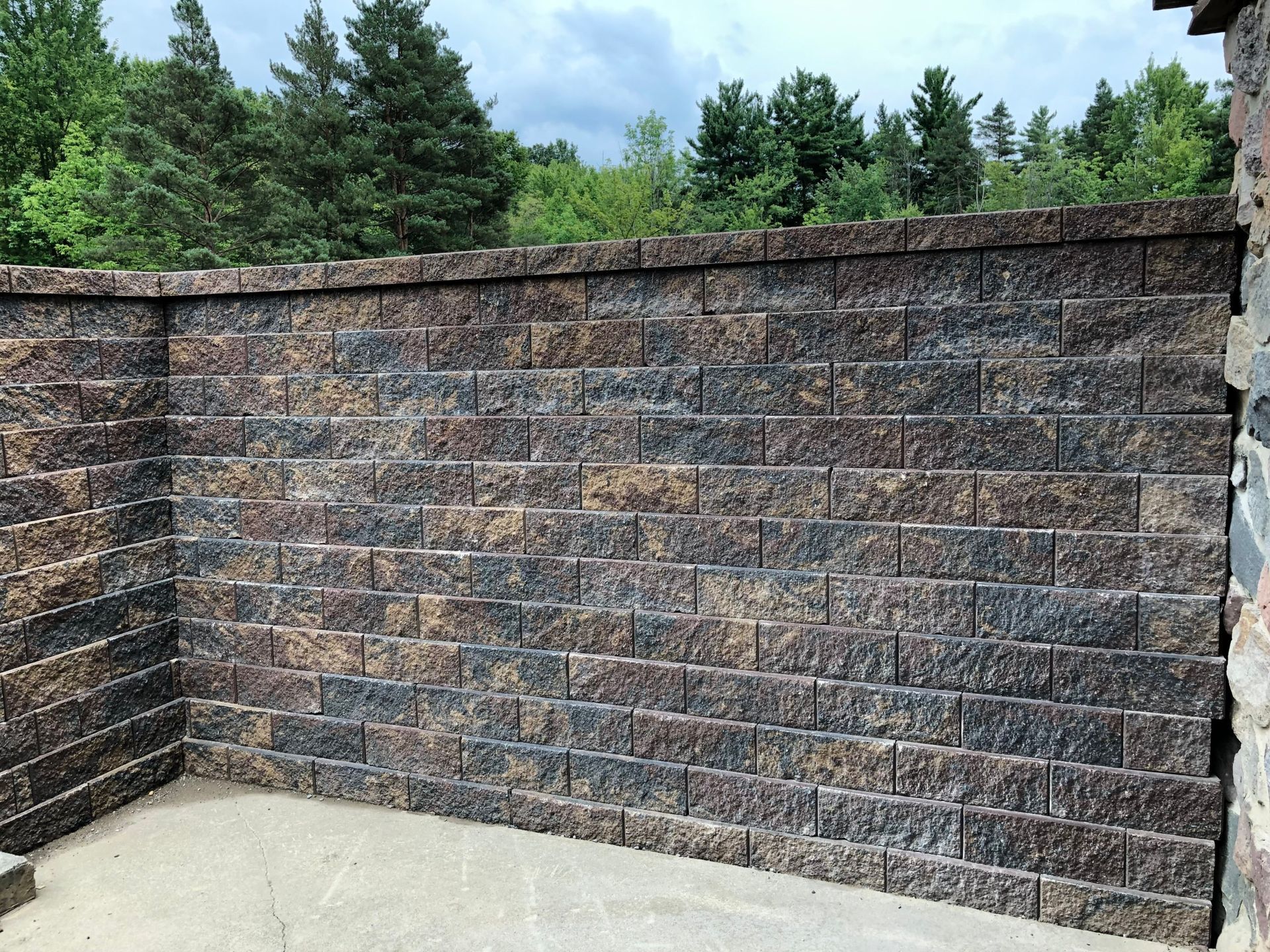 A brick wall with a patio in front of it and trees in the background.