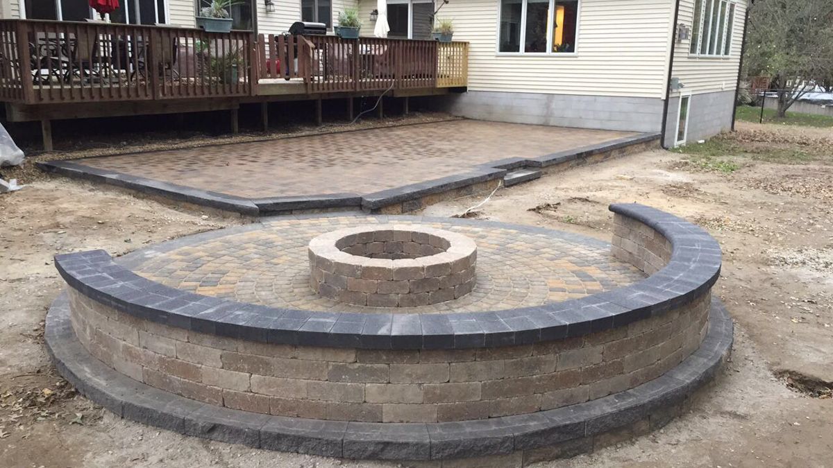 A fire pit is sitting in the middle of a patio next to a house.