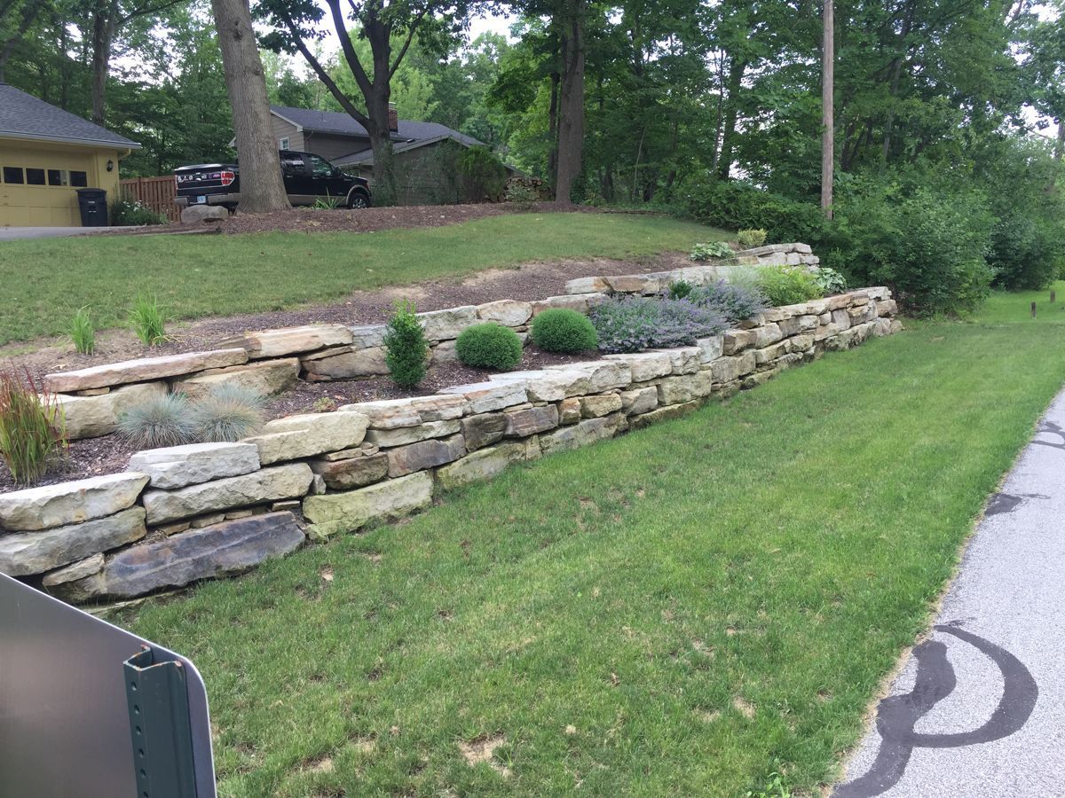 A stone wall surrounds a lush green lawn in front of a house.