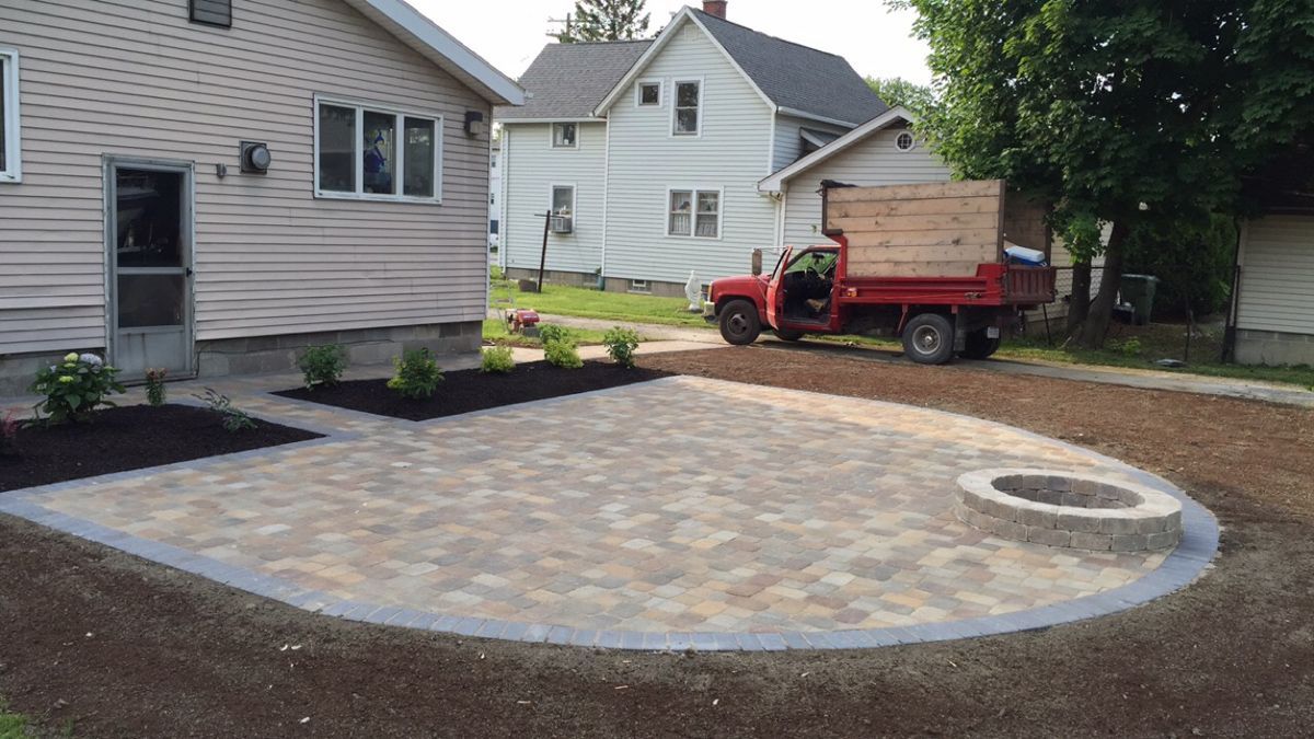 A red truck is parked in front of a house next to a fire pit.